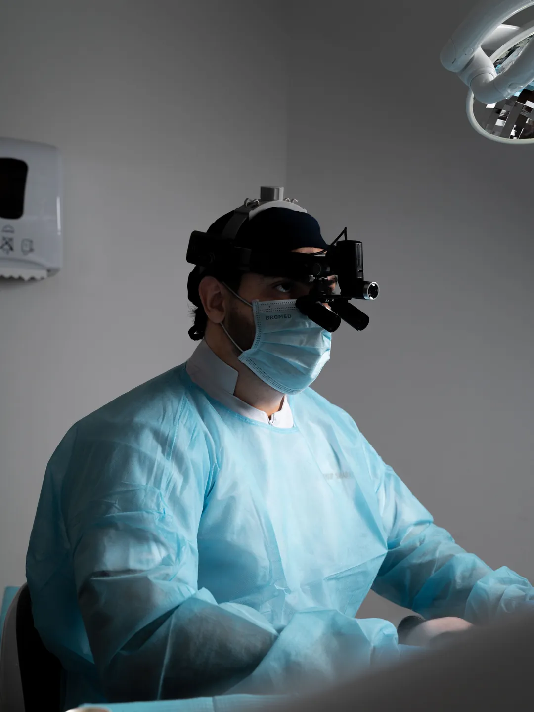 Cirujano oral con lupas quirúrgicas, luz frontal y bata estéril preparado para una intervención